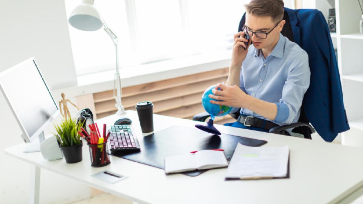 young_man_sits_office_computer_desk_talking_phone_looking_globe_88135_10465_26769600