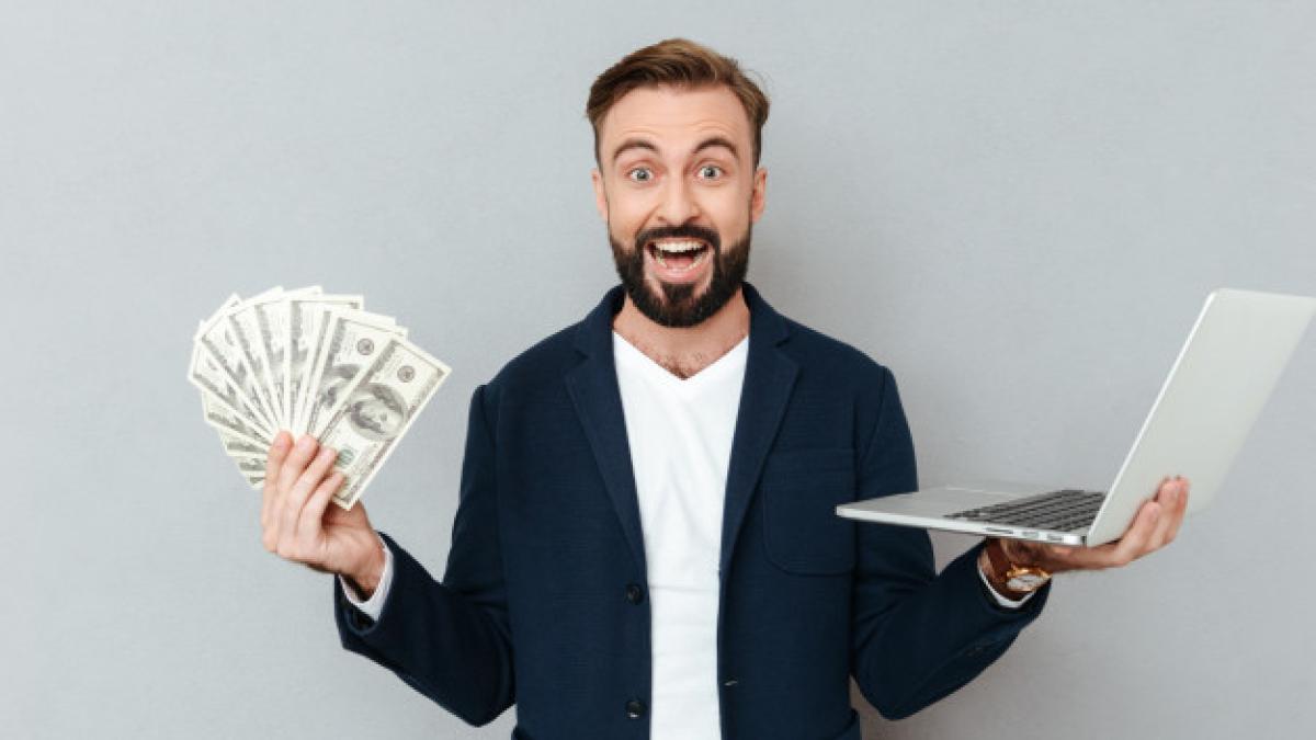 happy_surprised_bearded_man_busines_clothes_holding_money_laptop_computer_while_looking_camera_gray_171337_11359_40755600