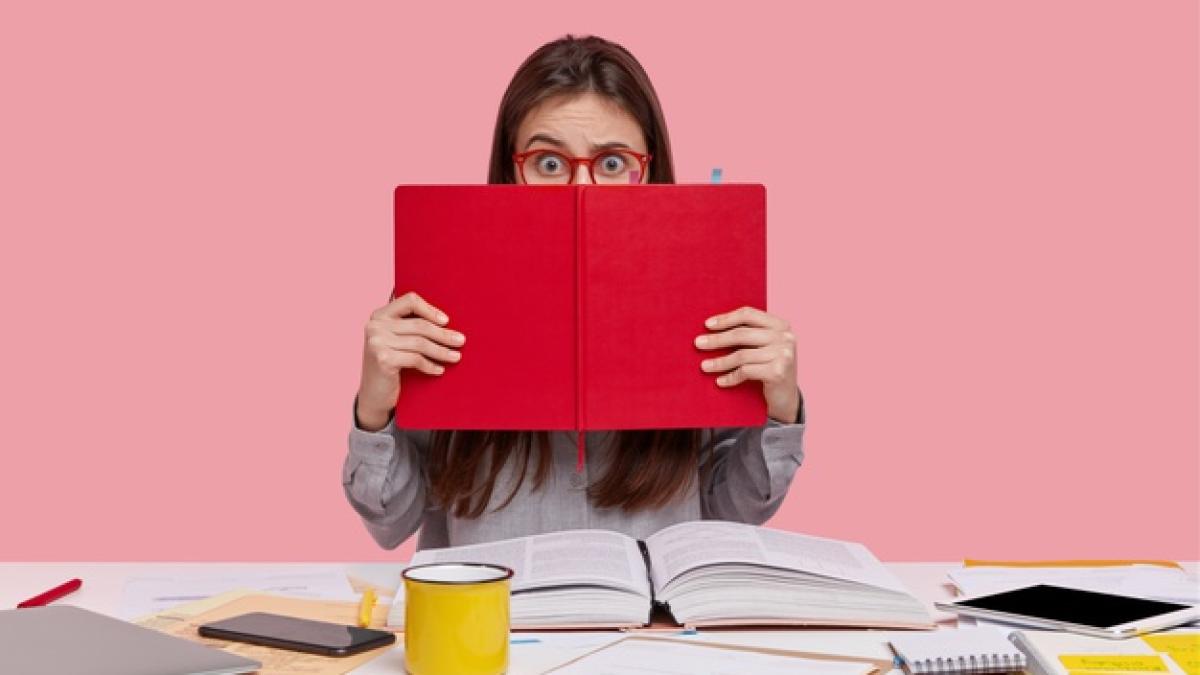 horizontal-shot-scared-puzzled-lady-covers-face-with-red-textbook-uses-modern-technologies_273609-24103_45359700