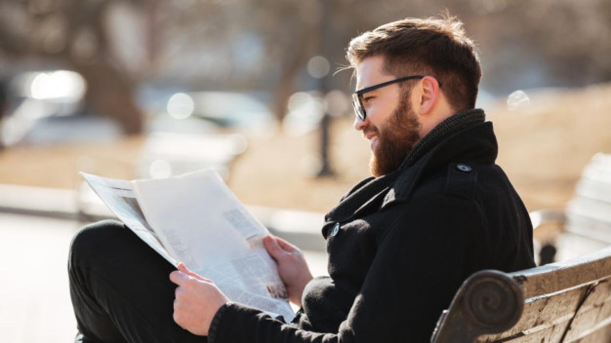 smiling-man-glasses-reading-newspaper-bench-outdoors_171337-14811_91396000