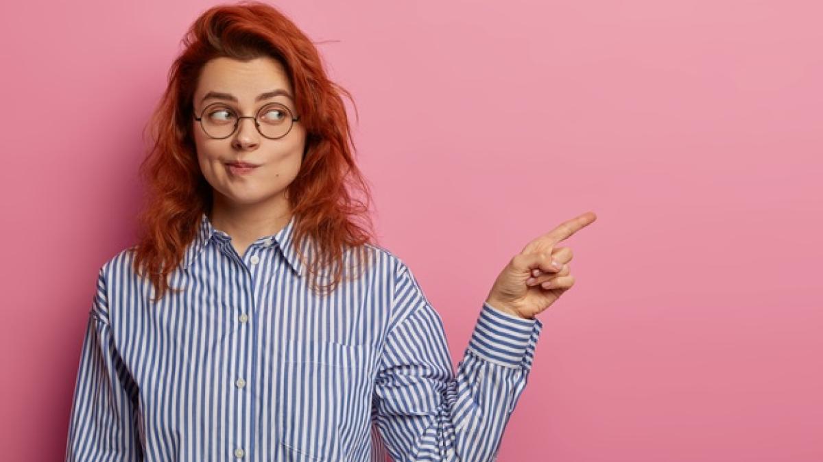 horizontal-shot-european-ginger-woman-purses-lips-demonstrates-something-blank-space-points-index-finger-aside_273609-38976_93537300