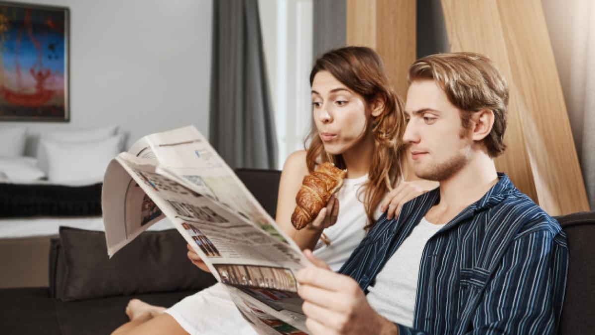 indoor_portrait_cute_couple_love_reading_newspaper_apartment_sitting_couch_wearing_pyjamas_girlfriend_reads_horoscope_page_eats_croissant_while_boyfriend_checks_business_news_176420_8686_82373700