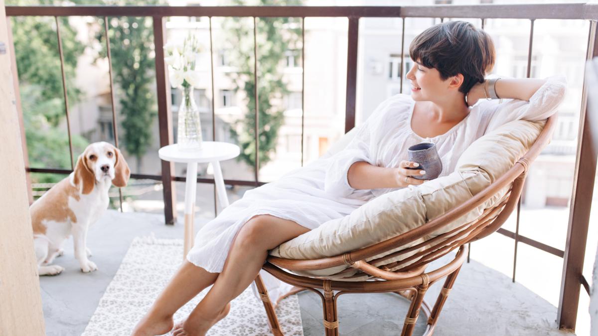 relaxed-barefooted-girl-white-dress-sitting-chair-balcony-holding-cup-tea-1_77673200
