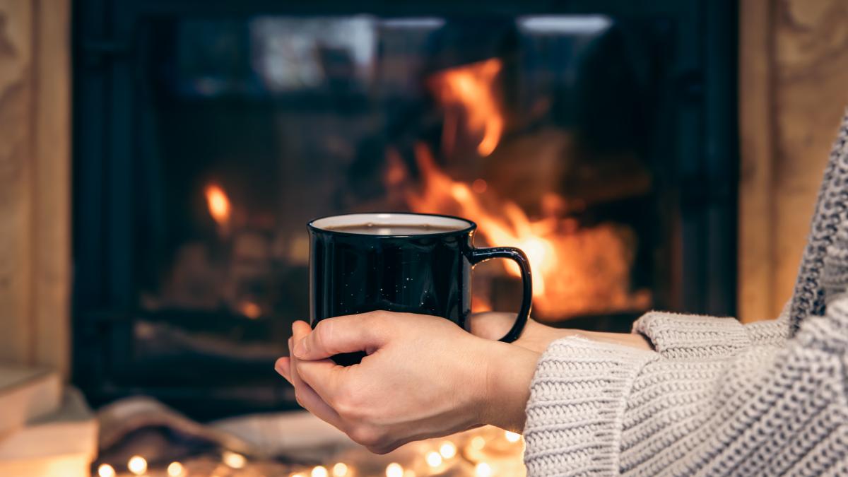 cup-with-hot-drink-female-hands-blurred-fireplace-background_62767600