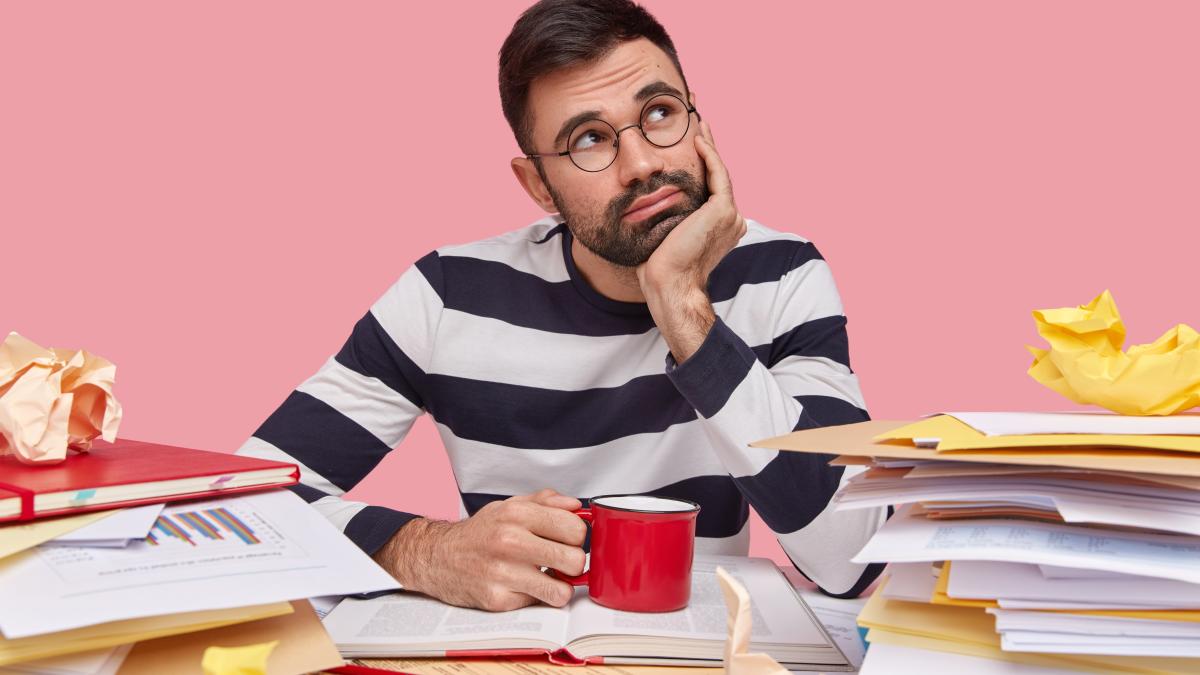 thoughtful-young-man-has-contemplative-expression-holds-hand-chin-wears-striped-jumper-drinks-fresh-beverage-surrounded-with-pile-textbooks_67013300