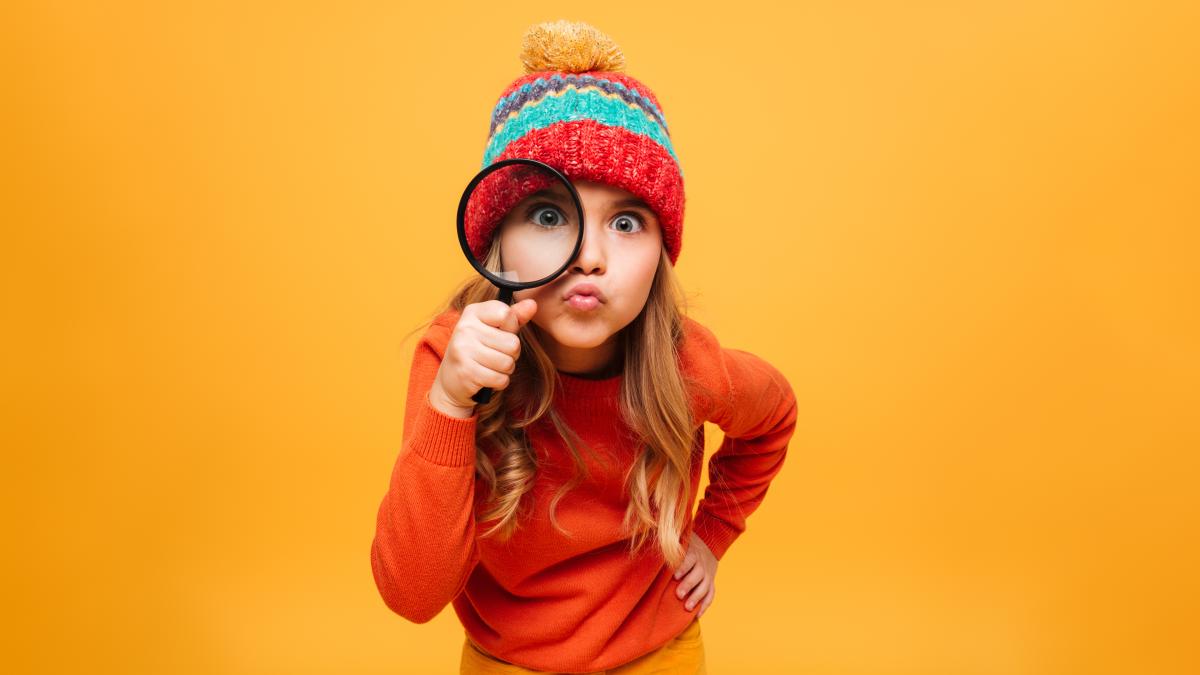 joyful-young-girl-sweater-hat-looking-camera-with-magnifier-orange_02664700