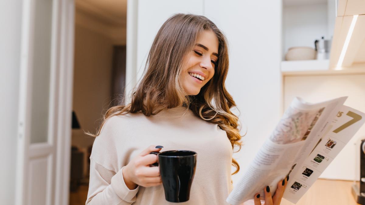 glad-white-woman-beige-attire-reading-news-kitchen-while-drinking-coffee_91276400