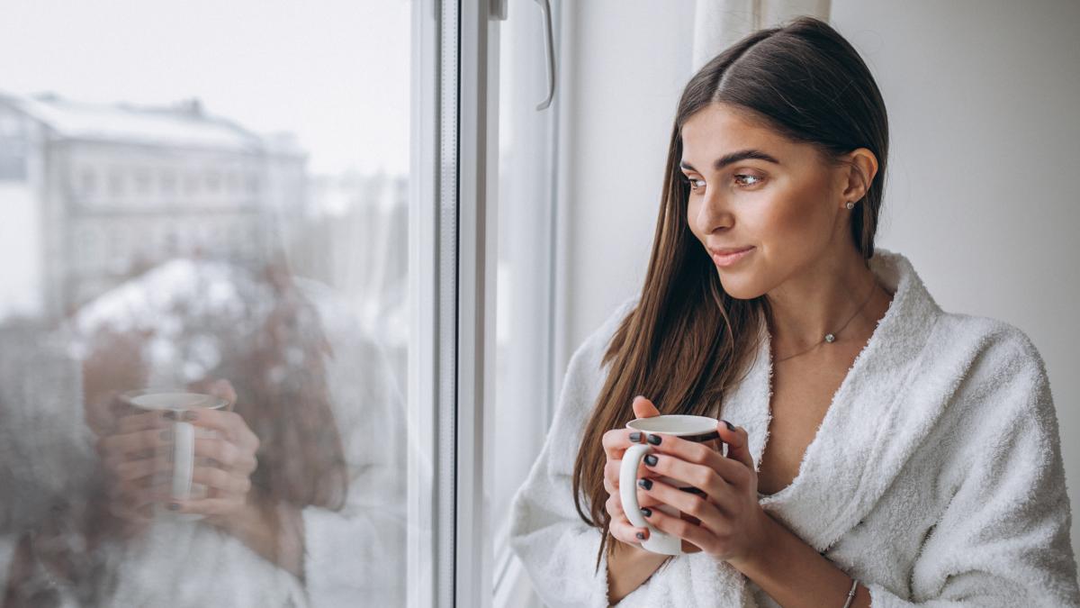 young-woman-standing-by-window-drinking-hot-coffee_53531700