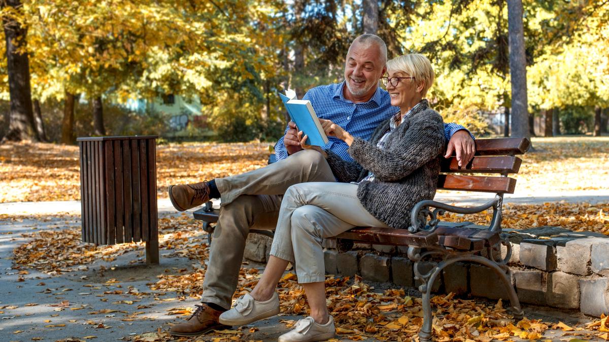 caucasian-elderly-couple-sitting-bench-reading-book-park_38080700