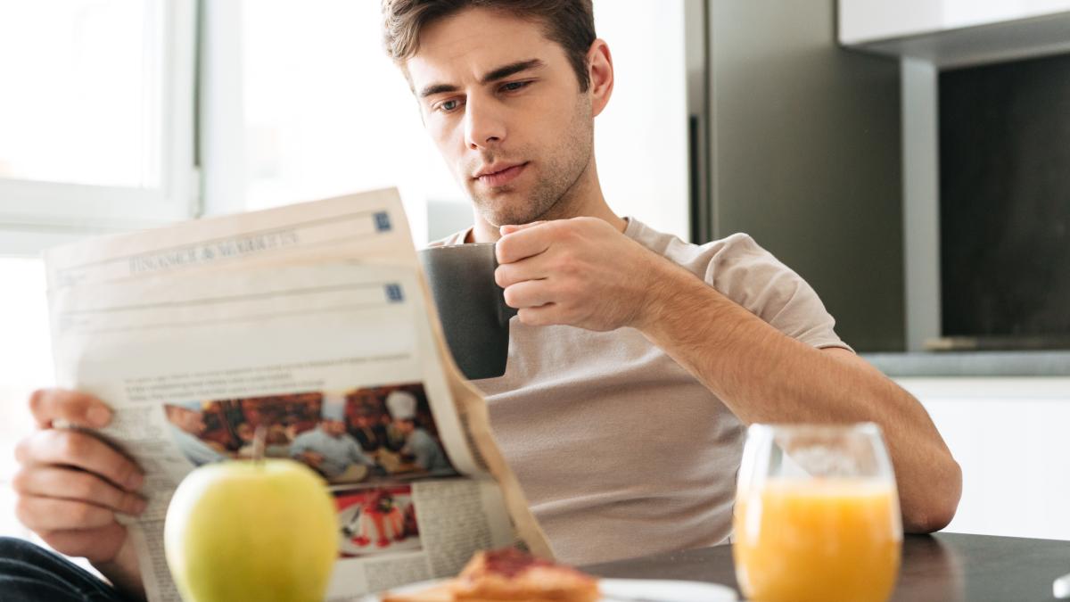 young-concentrated-man-reading-newspaper-while-sitting-kitchen_68584500
