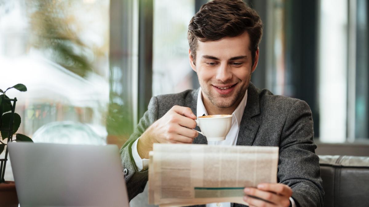 smiling-businessman-sitting-by-table-cafe-with-laptop-computer-while-reading-newspaper-drinking-coffee_11521100