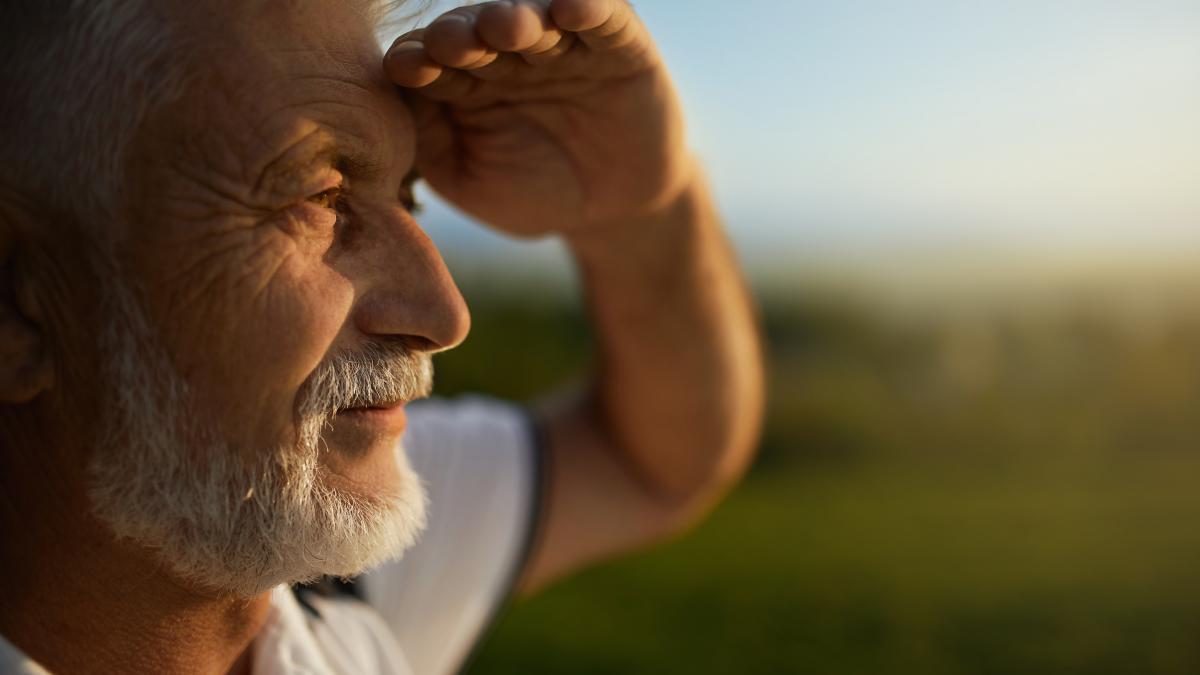 bearded-man-squinting-from-bright-sun-while-looking-into-distance-during-trip_78127900