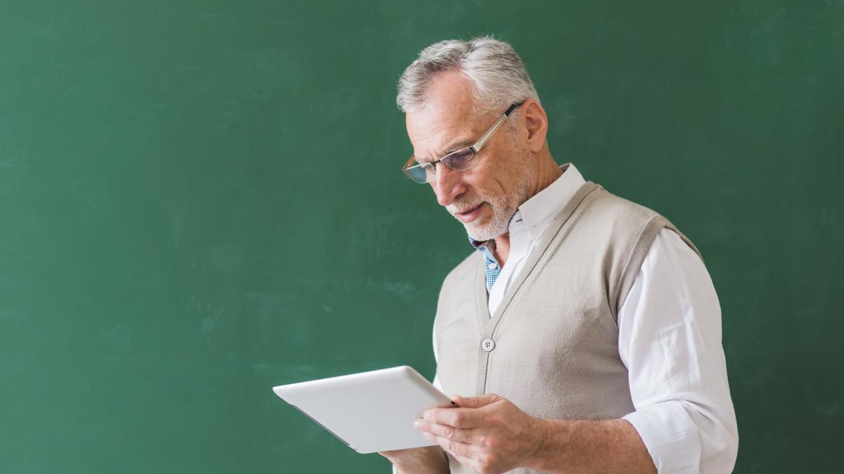 senior-male-professor-using-tablet-near-chalkboard_80425400