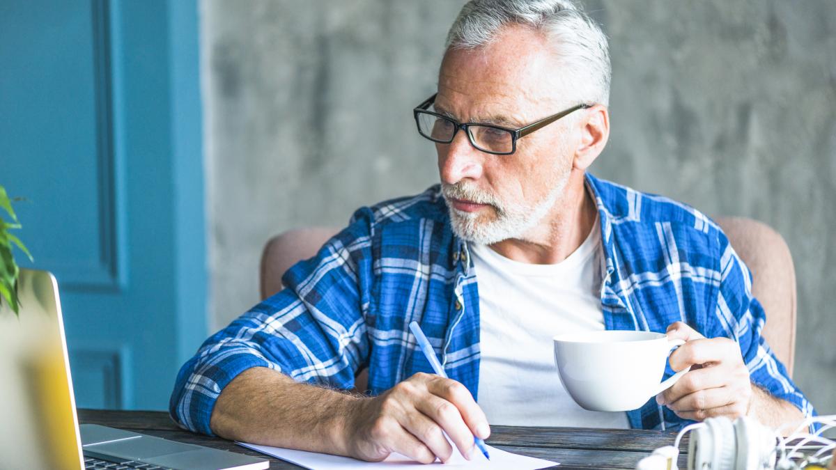 senior-man-looking-laptop-holding-pen-making-notes_91604600