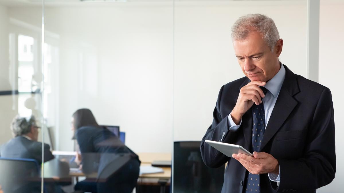 focused-pensive-businessman-staring-tablet-screen-while-his-colleagues-discussing-project-workplace-glass-wall-copy-space-communication-concept_85717800