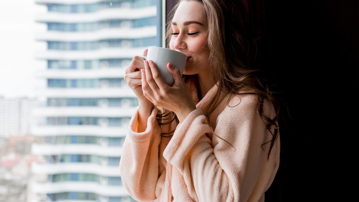 fresh-young-woman-pink-tender-bathrobe-drink-tea-looking-out-window_20660600