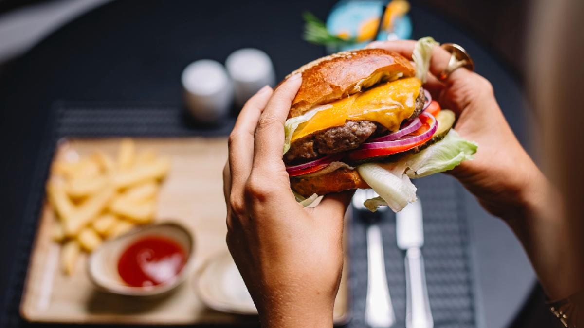 woman-holds-beef-burger-with-lettuce-tomato-red-onion-cheddar-cheese_06181800