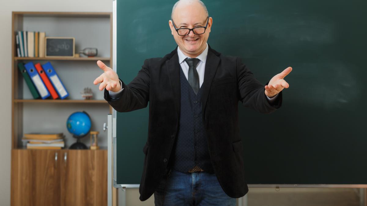 man-teacher-wearing-glasses-standing-near-blackboard-classroom-explaining-lesson-making-welcoming-gesture-with-hands-smiling_20941500