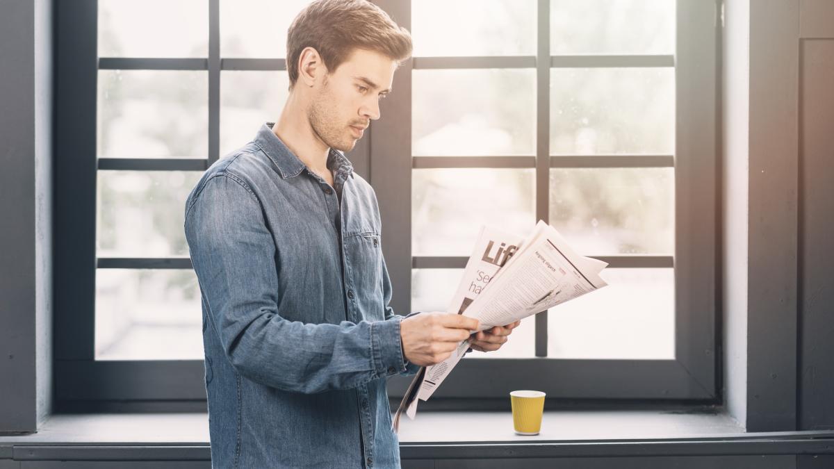 man-standing-near-closed-window-reading-newspaper-1_15680000