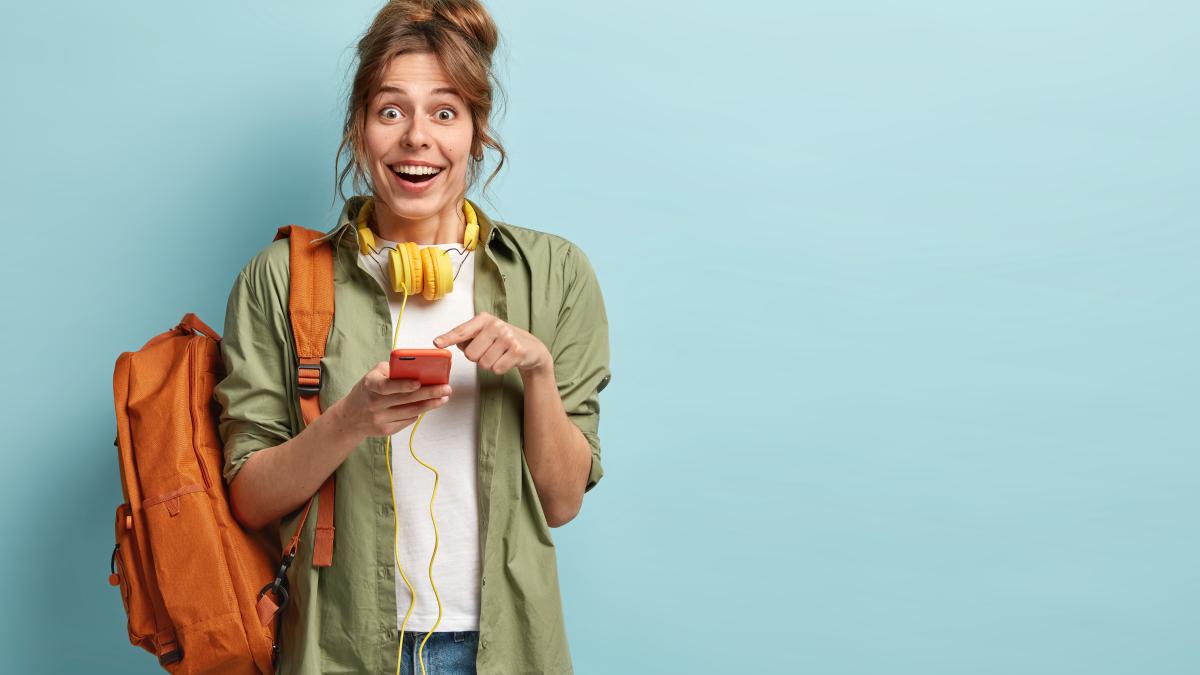 joyous-hipster-girl-feels-excited-chatting-with-friends-watches-funny-video-new-gadget-points-screen-has-headphones-neck_46029600