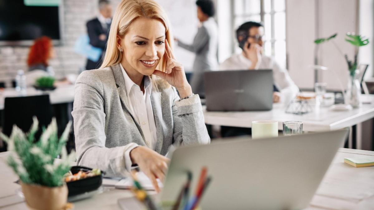 happy-mid-adult-businesswoman-using-computer-surfing-internet-while-working-office-there-are-people-background_11223300