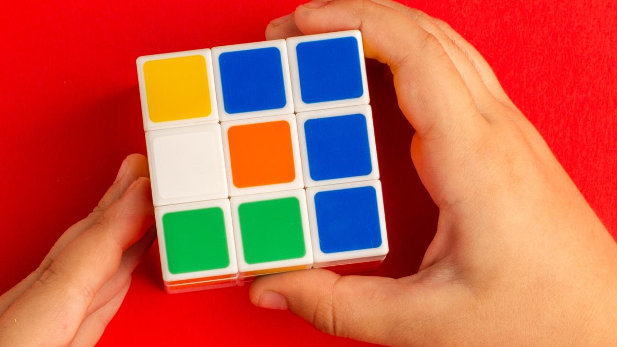 top-view-little-kid-playing-with-rubics-cube-red-desk_00954400