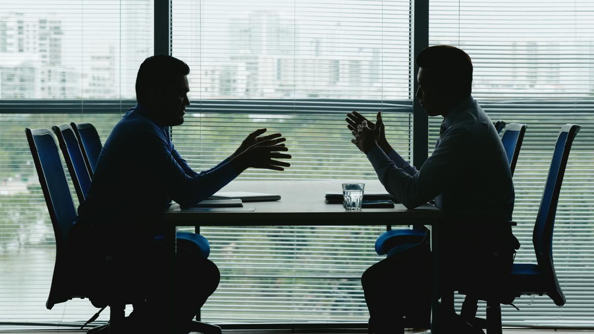 two-human-outlines-against-shuttered-office-window-sitting-opposite-each-other-negotiating_67313500