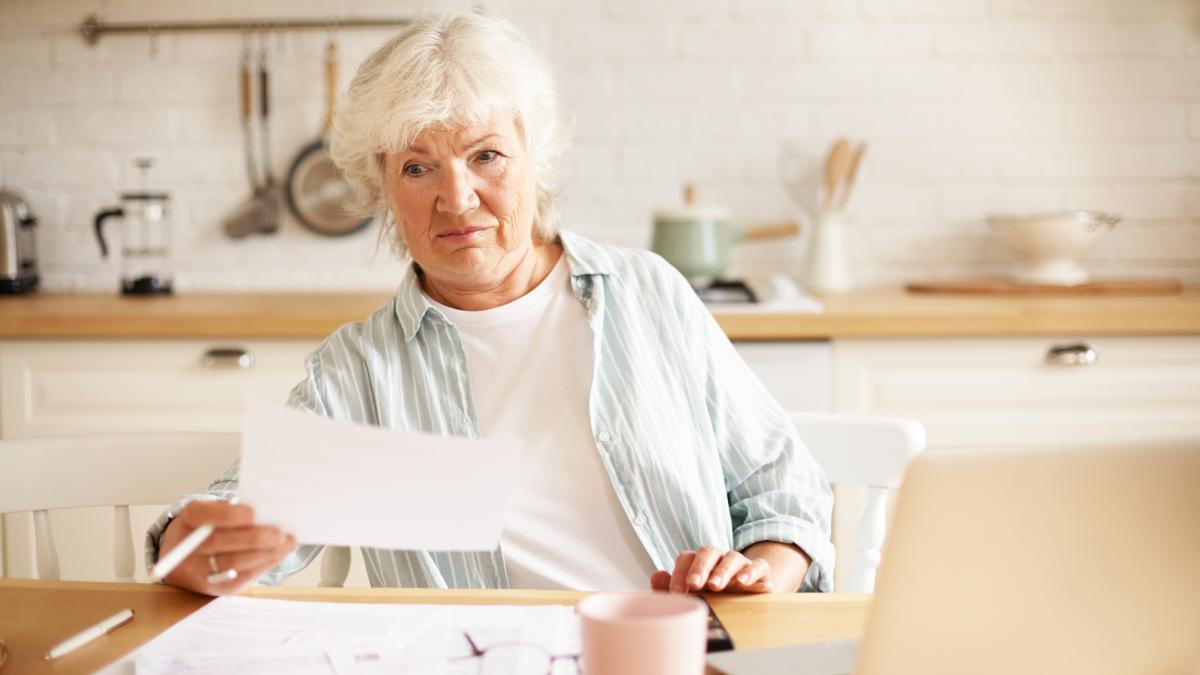 elderly-housewife-with-gray-hair-sitting-kitchen-with-open-laptop-papers-table-having-emotional-frustrated-facial-expression-shocked-with-debt-amount-while-paying-domestic-bills-online_66144400