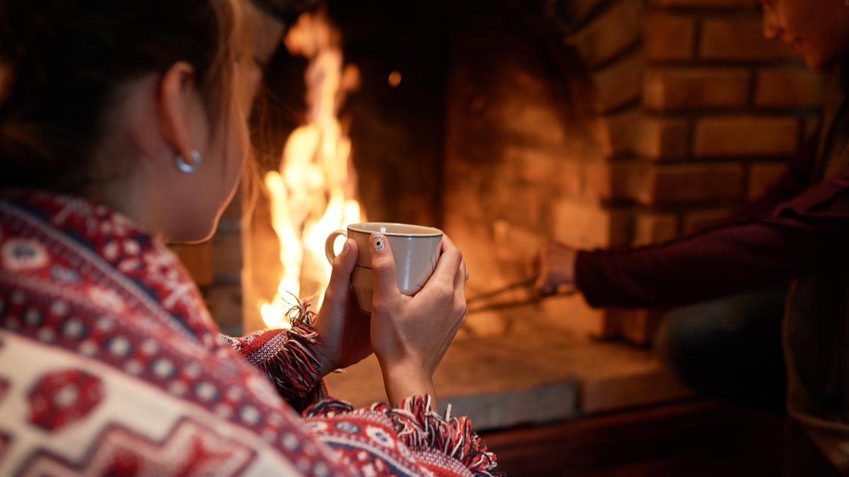 shoulder-shot-woman-warming-her-hands-mug-hot-tea-sitting-fireplace-her-boyfriend-dealing-with-charcoal_48203300
