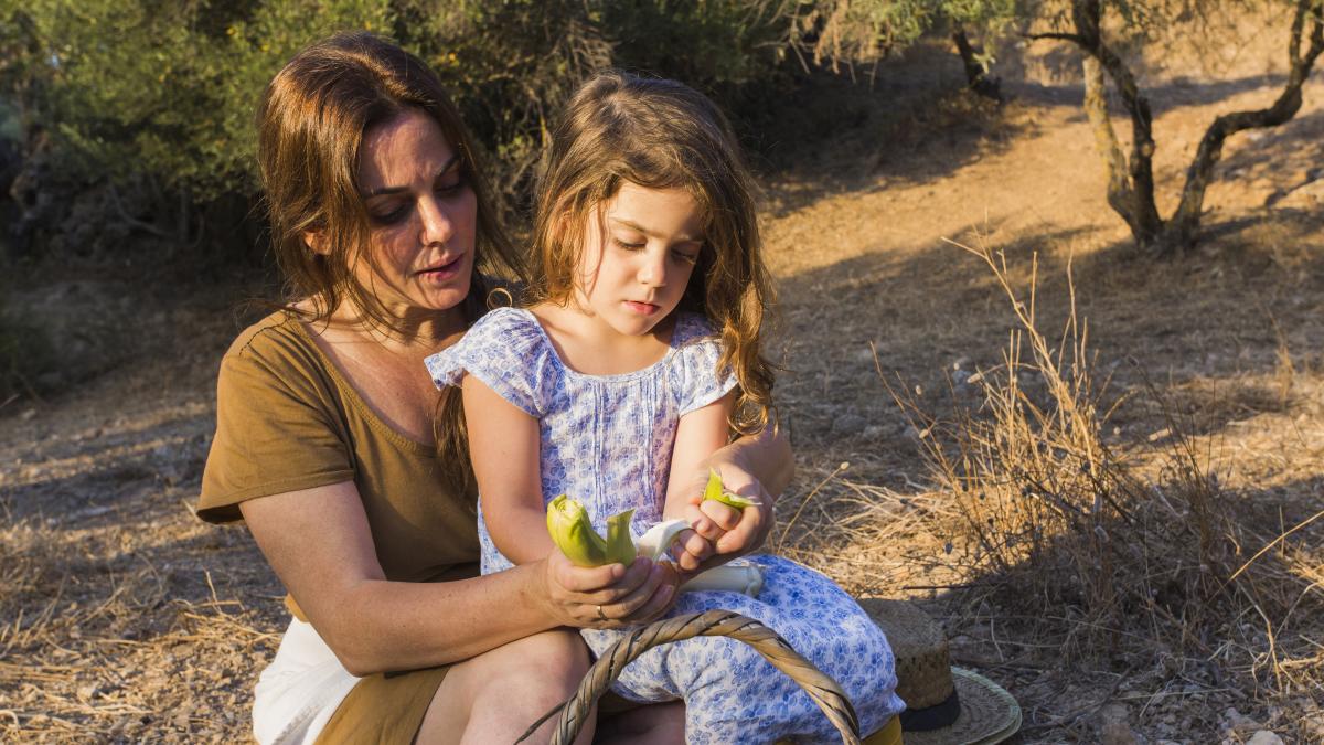 daughter-sitting-mother-s-lap-holding-leek-field_96080200