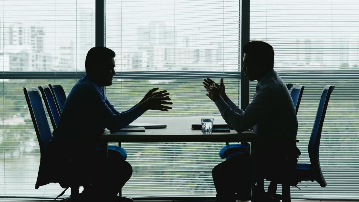 two-human-outlines-against-shuttered-office-window-sitting-opposite-each-other-negotiating_93466400