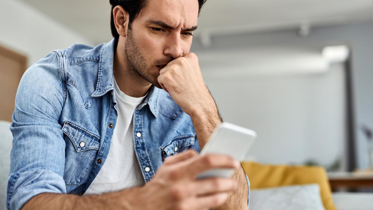 young-man-feeling-worried-while-reading-text-message-mobile-phone-home_57970500