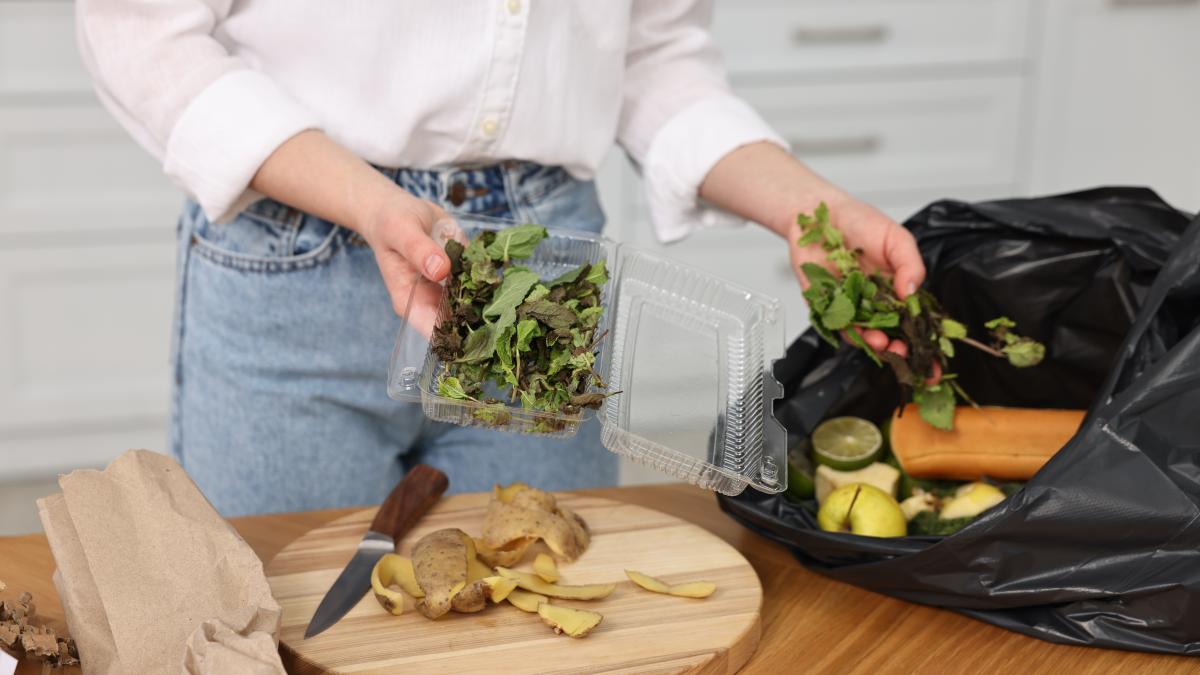 garbage-sorting-woman-putting-food-waste-into-plastic-bag-wooden-table-indoors-closeup_17512200
