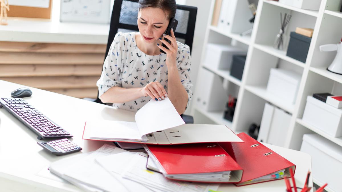 young-girl-sitting-office-computer-desk-working-with-documents-talking-phone